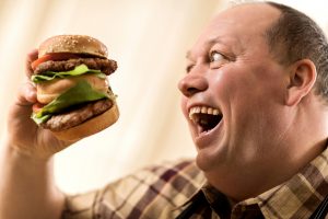 Overweight excited man about to eat a huge hamburger.